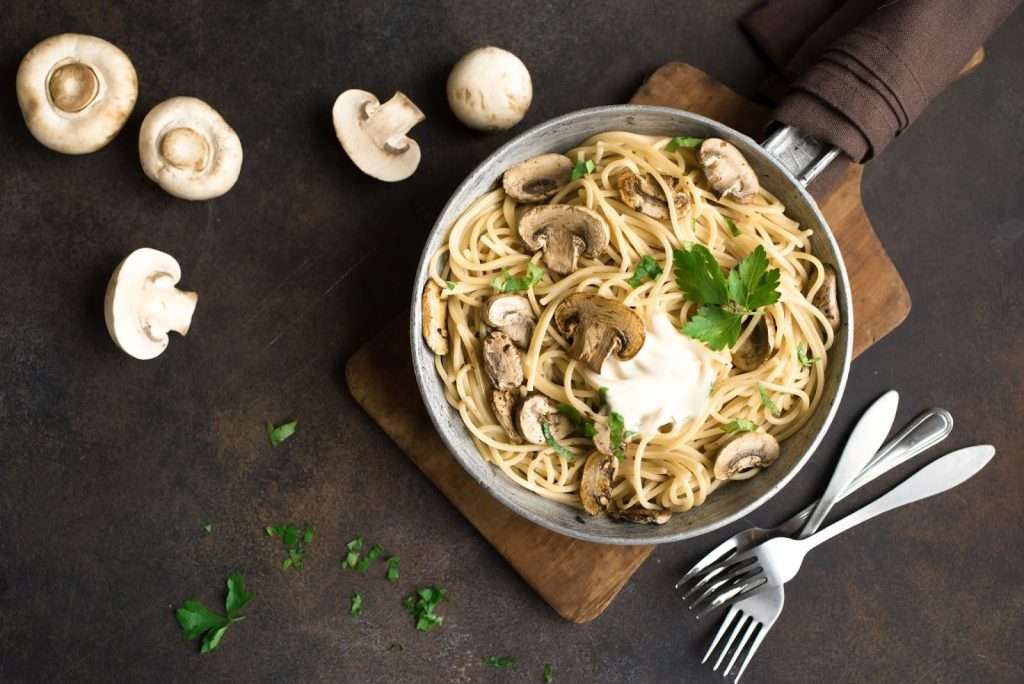 Creamy vegan mushroom pasta with spaghetti, fresh mushrooms, parsley, and plant-based cream in a skillet
