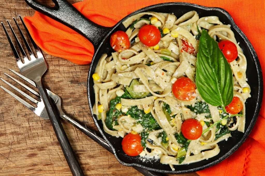 Creamy vegan pasta skillet with cherry tomatoes, spinach, corn, basil, and plant-based parmesan
