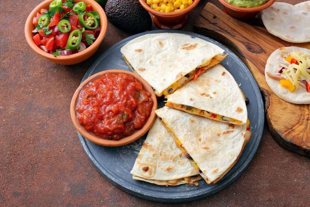 Vegan quesadilla with plant-based cheese, black beans, corn, peppers, salsa, avocado, guacamole, and pico de gallo