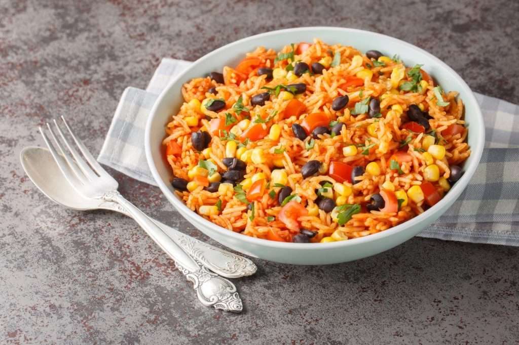 Vegan Mexican rice bowl with black beans, corn, tomatoes, cilantro, and red peppers served in a white bowl
