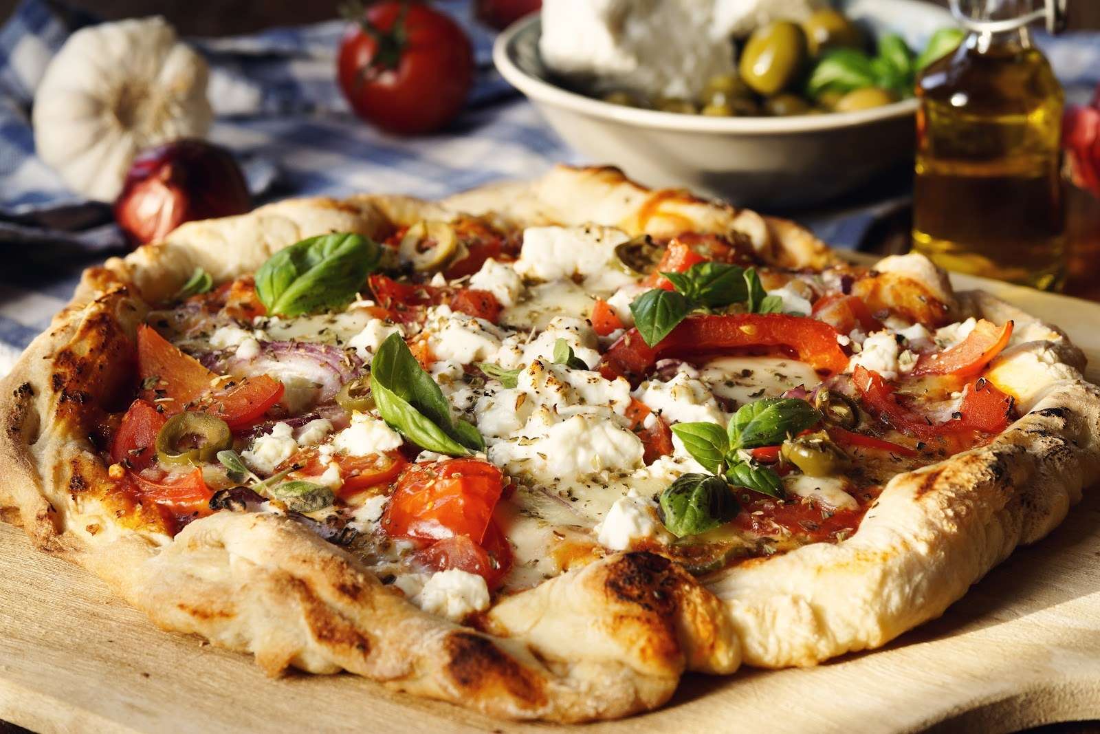 A quick and easy vegan pizza with a thick, golden crust topped with melted vegan mozzarella, crumbled plant-based feta, tomatoes, green olives, and fresh basil leaves.
