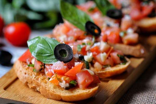 Vegan bruschetta with diced tomatoes, basil, black olives, and herbs on toasted bread slices

