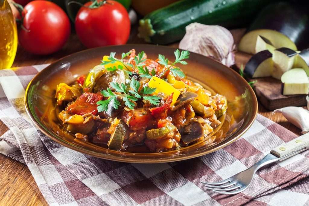 Vegan ratatouille with eggplant, zucchini, bell peppers, tomatoes, garlic, and fresh parsley in a bowl