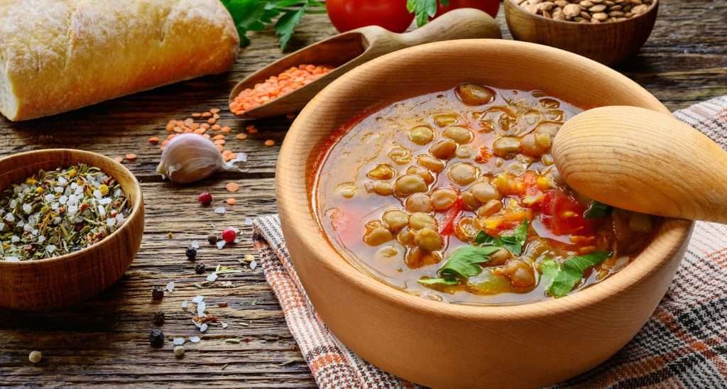 Hearty vegan lentil soup with tomatoes, herbs, garlic, and bread served in a wooden bowl
