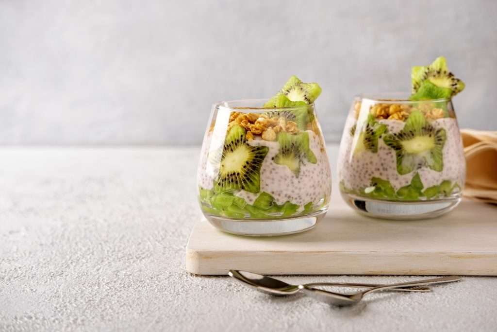 Vegan kiwi chia pudding parfaits with granola served in glass cups on a white tray