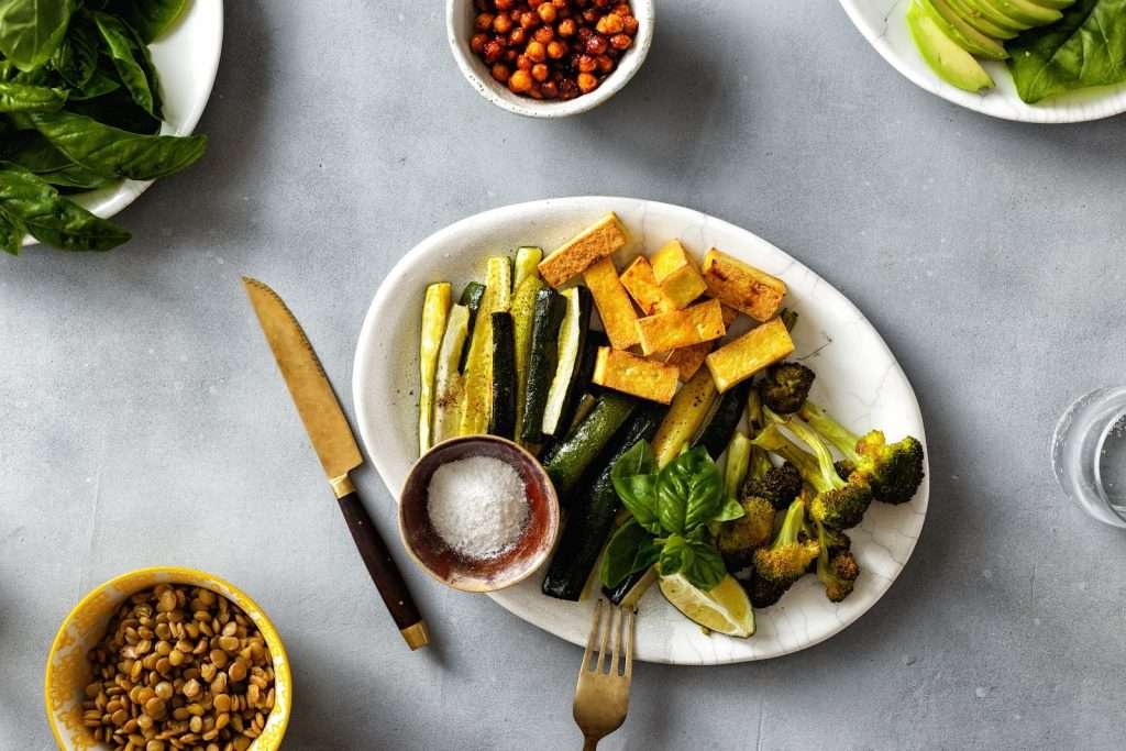 Roasted vegan tofu and vegetable plate with zucchini, broccoli, lentils, crispy chickpeas, avocado, basil, and lime