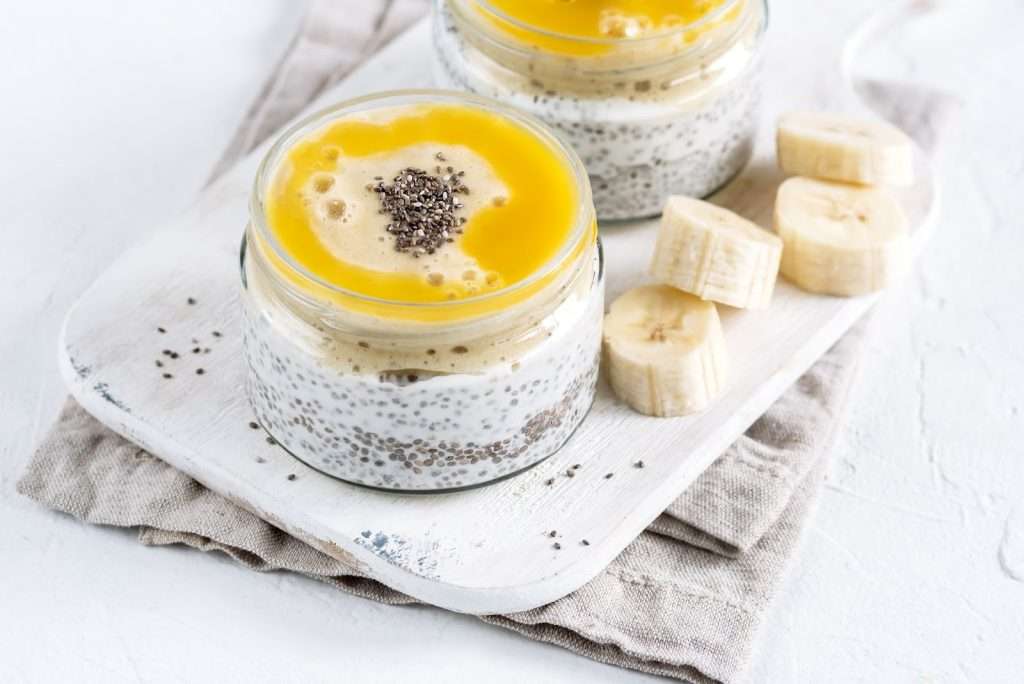 Vegan chia pudding jars with mango topping, banana slices, and chia seeds on a white serving board