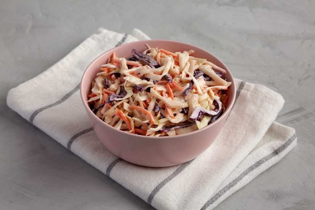 Creamy vegan coleslaw with shredded cabbage, carrots, and red cabbage served in a pink bowl