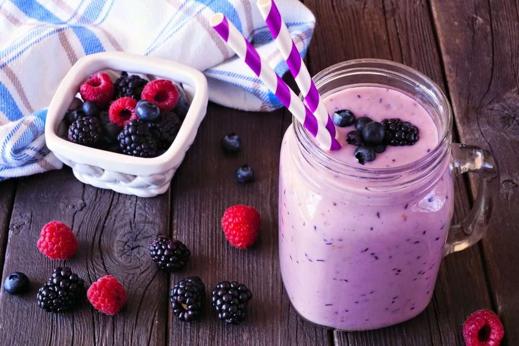 Vegan berry smoothie in a mason jar with raspberries, blackberries, blueberries, and striped straws on a wooden table