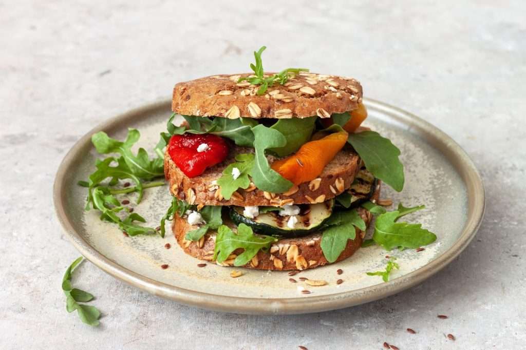 Vegan grilled vegetable sandwich with arugula, roasted zucchini, carrots, red pepper, and seeded whole grain bread
