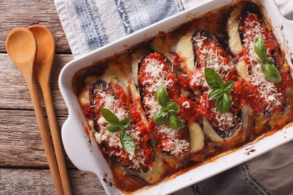 Vegan baked eggplant casserole with tomato sauce, basil, and plant-based cheese in a white baking dish
